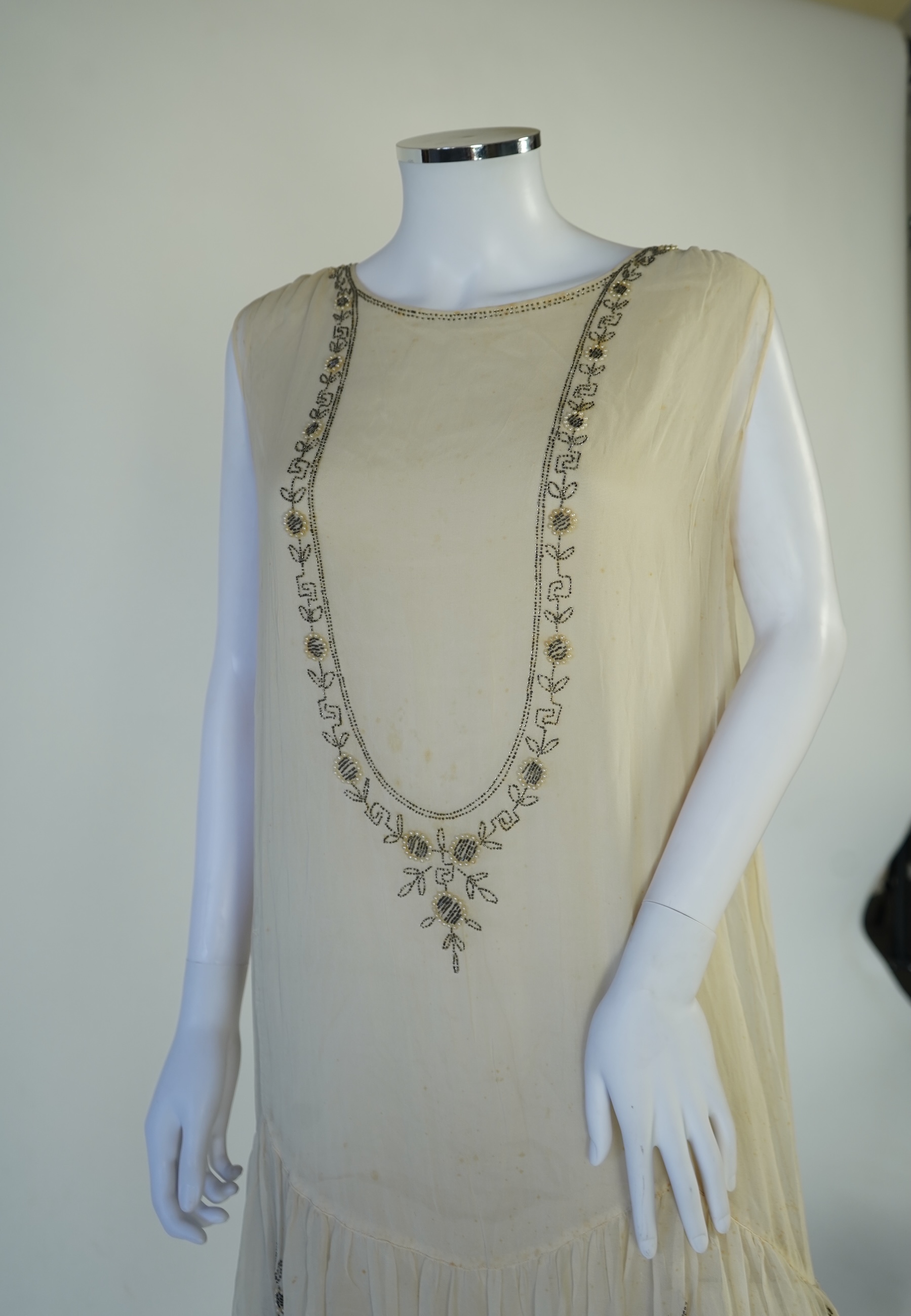 A 1920's cream silk georgette three quarter length, silk lined ‘flapper dress’. Designed with beaded and pearl floral embroidery, a stylish long beaded keyhole slit at the back, a beaded front bodice and flying beaded pa